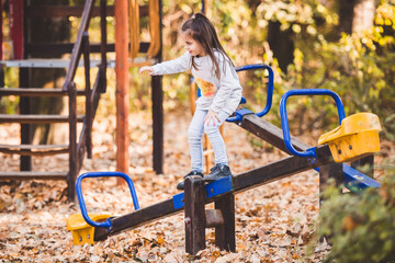 Little girl balancing on seesaw in playground during autumn