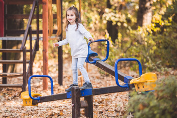 Cute little girl balancing on seesaw in playground during autumn