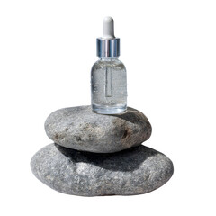Clear glass dropper bottle with serum resting on stacked grey stones isolated on transparent background