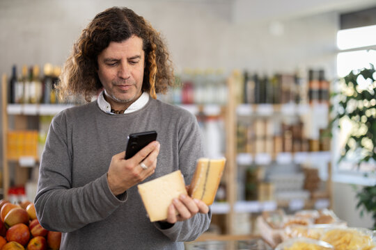 Adult man scans a barcode of a cheese package on his mobile. Buyer scans the QR code on his phone to pay at the supermarket checkout