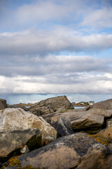 Rugged Nordic Coastal Landscape: Foreground Boulders Frame Distant Village & Sea Under Dynamic Cloudy Sky - Serene Shoreline