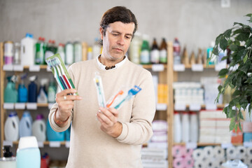 Male buyer looks through product options near open store display. Store visitor chooses toothbrush,...