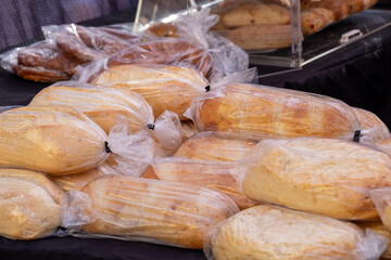 A display of artisan breads in clear plastic bags for sale at a farmer's market. The crusty,...