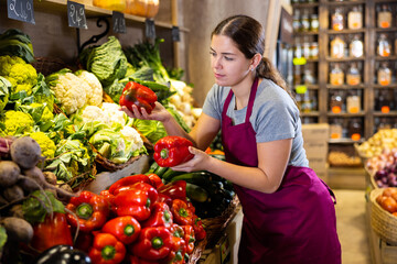 Saleswoman near fruit and vegetables stalls offering to buy paprika