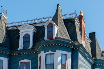 The top corner floor of a teal green wooden house with red and white trim. The building has a...