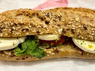 close-up of a cereal bread sandwich with goat cheese slices, tomato slices and salad
