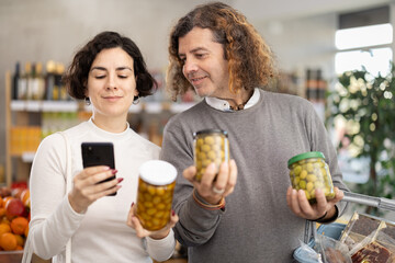 Couple scans barcode QR code on pickled olives label package, follows link and studies information...