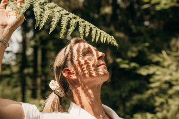 Woman in forest lifting fern leaf above her head, close-up nature shot