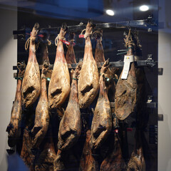 Traditional cured ham legs hanging on metal rack in delicatessen store interior