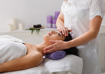 Head relaxing massage in spa. Female beautician doctor with patient in wellness center. Professional cosmetologist make procedure to beautiful indian girl in cosmetology cabinet or beauty parlor.