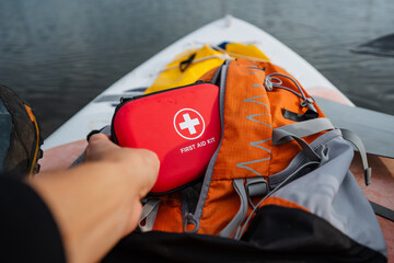 A person is carefully placing a first aid kit into their backpack, ensuring it is secured and...