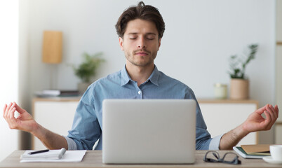Office Zen. Relaxed Young Man Meditating Sitting At Laptop Computer At Workplace.