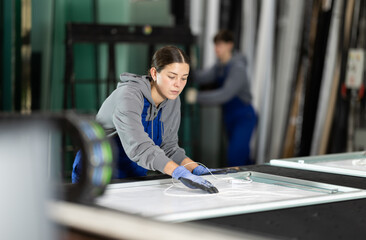 Young woman worker in uniform puts sheet of glass on table for processing in glass factory