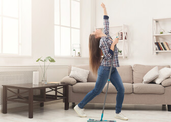 Happy woman cleaning home, singing at mop like at microphone and having fun, copy space. Housework,...