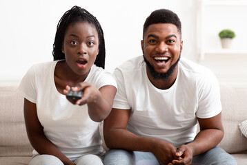Shocking tv programm. Surprised black couple watching tv with opened mouth, switching channels at...