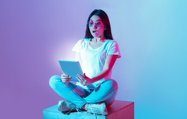 Shock at information received. Young asian woman in glasses sits in lotus position and holds tablet...