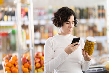 Adult woman buyer scanning qr code for olives in jar in grocery store
