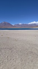 Expansive view of Lagunas Miñiques and Miscanti, a high-altitude turquoise lagoon in a vast Atacama desert landscape with the majestic Andes mountains under a clear blue sky. 