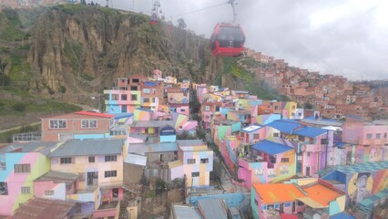 Aerial view from a cable car showing Chualluma, a colorful favela with painted houses and street art on a steep hillside. Urban public transportation system in La Paz, Bolivia, on a foggy day.