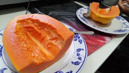Close-up of a fresh ripe papaya cut in half on a decorative plate. Another plate with a slice of...