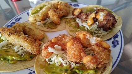 Close up of a plate with delicious homemade shrimp and fish tacos, featuring crispy breaded seafood, fresh guacamole, shredded cabbage, and a creamy chipotle sauce on corn tortillas.