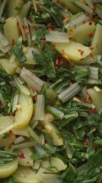 Background pattern of South Croatian Blitva s Krumpirom dish. The dish is made with boiled potatoes, swiss chard, garlic, and olive oil. Table spin, vertical video.