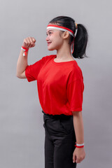 Side view of a young woman wearing a red shirt and red-white headband, smiling with raised fist, showing determination, joy, and spirit of Indonesian Independence Day celebration.