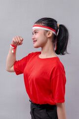 Close-up side view of a young Indonesian woman smiling proudly with a clenched fist, wearing red...