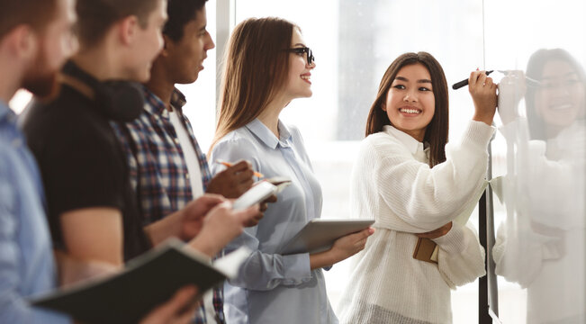 Students discussing tasks on whiteboard in classroom and making notes, panorama