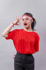 Excited young Indonesian woman in red showing an OK hand gesture with open mouth expression,...