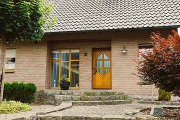 The entrance of the charming brick house features a beautifully designed wooden door surrounded by...