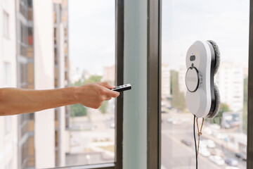 Close-up cropped shot of housekeeper using remote controller to operate robotic window cleaner, ensuring efficient and safe cleaning of high-rise building windows with cityscape view.