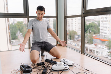 Confused worker crouching among tangled window cleaning robot cables, troubleshooting technical setup near expansive glass windows in living space. Concept of cleaning house with smart devices.