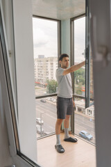 Full length vertical shot of cleaning company worker cleaning large window with professional squeegee, revealing city street view, maintaining spotless surface in contemporary workplace setting.