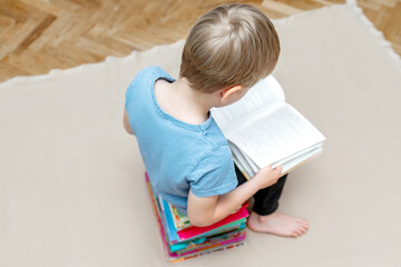 Little boy kid child sitting on stack of children's books and leafing through a book with pictures of fairy tales,learning read.Education