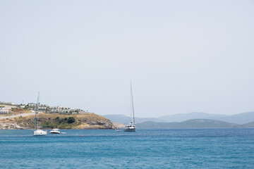 Sailboats navigating calm waters near a coastal hillside in bright daylight
