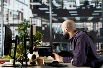 Middle eastern manager in modern office examines infographics to oversee business operations,...