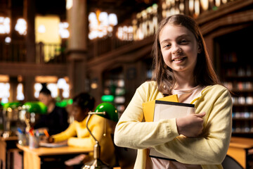 Portrait of a cute schoolgirl working on a project in the school library, using the academic database for homework research. Preteen student solving her school assignments for higher grades.