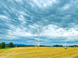 An isolated wind turbine stands gracefully in an expansive open field beneath a dramatic sky that...