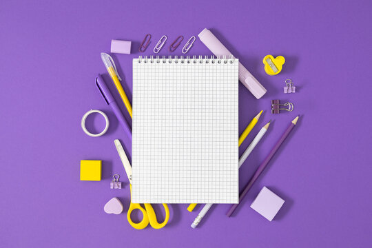 Back to school composition, open notebook, yellow and purple school supplies and stationery on purple background.