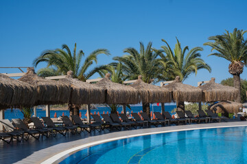 Relaxing day at a tropical resort poolside with thatched umbrellas and palm trees by the sea