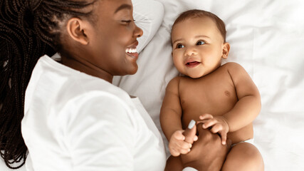 Unconditional Love. Closeup portrait of positive African American woman lying with her cute little black baby on bed, smiling and spending time with infant kid in bedroom at home. Happy Family