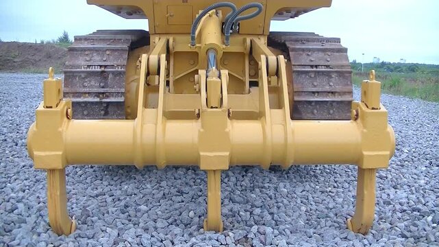 Bulldozer raised on ripper during active movement tracks, close-up of powerful hydraulic ripper system engaged in soil work, selective focus. Concept of construction, mining, heavy machinery.