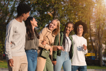 International group of cheerful teenagers laughing while walking by golden park
