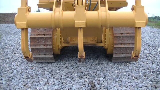 Heavy machinery ripper lifting up from crushed stone surface, bulldozer with track system working on site, selective focus. Concept of construction industry, mining operations, road building.