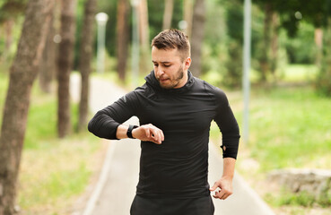 Morning Routine Concept. Portrait of handsome guy running in parkland, checking heart rate on his...