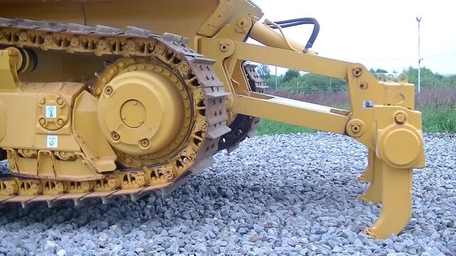 Rotating tracks of yellow bulldozer lifted on ripper attachment working on gravel construction site, selective focus. Concept of construction, earthworks, heavy equipment rental.