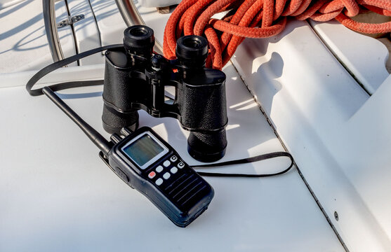 A handheld VHF marine radio and binoculars on a sailboat table