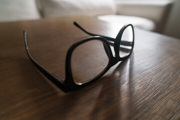Black rimmed eyeglasses resting on wooden table in soft sunlight.