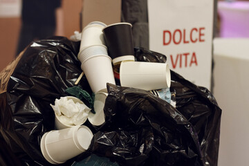 Trash many paper used cups in black bag and text dolce vita in background in blur